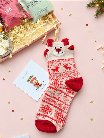 Red and cream festive socks beside a teddy pocket hug on its seasonal card.